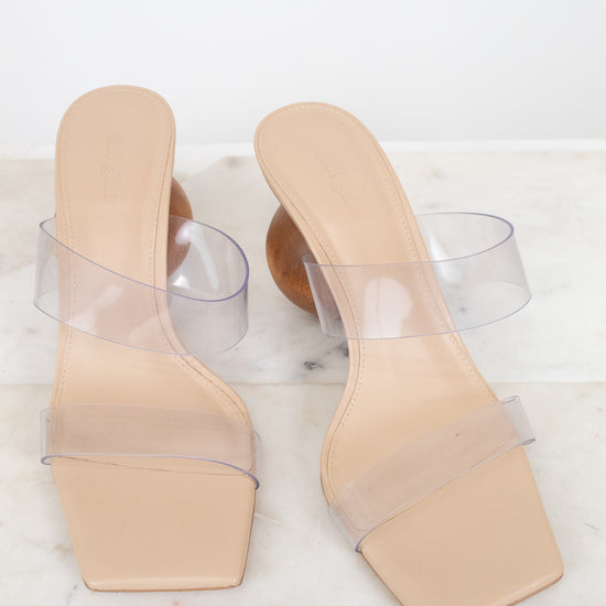Beige high-heeled shoes with clear straps on a white marble surface