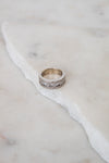 A silver band ring with a row of clear diamonds, resting on a white marble slab against a light marble background.