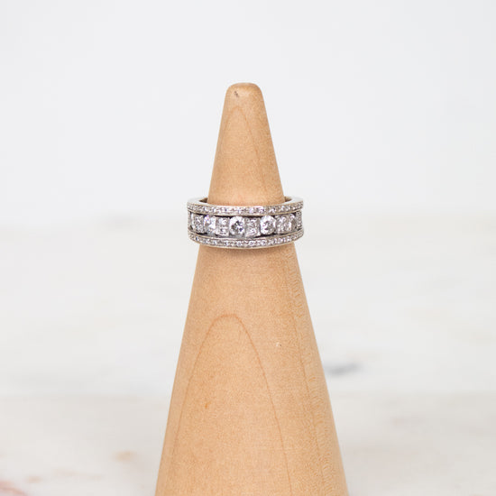 A silver band ring set with diamonds, displayed on a light wood cone stand against a white background.