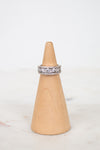 A silver band ring set with diamonds, displayed on a light wood cone stand against a white background.