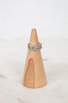 A silver band ring with diamonds, displayed on a light wood cone stand against a soft white background.