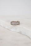 A silver band ring with multiple rows of diamonds, resting on a white marble slab against a soft light gray background.