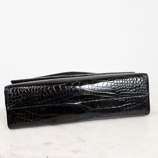 A black crocodile-embossed leather handbag, shown closed on a white marble surface against a white background.