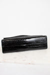 A black crocodile-embossed leather handbag, shown closed on a white marble surface against a white background.