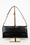 A black crocodile-embossed leather shoulder bag with gold-tone hardware, displayed on a gold metal stand against a white background.