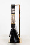 A black crocodile-embossed leather handbag with a wide, decorative strap featuring gold-tone hardware and a row of clear rhinestones, displayed on a gold metal stand against a white background.