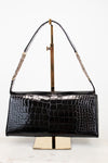 A black crocodile-embossed leather handbag with a gold-tone chain strap, displayed on a gold metal stand against a white background.