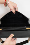 An open black handbag with gold-tone hardware, shown from the inside with two hands holding it open. The bag has a black interior lining and a black exterior with gold accents.