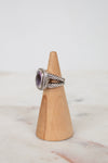 Silver ring with a purple gemstone on a wooden cone against a marble background