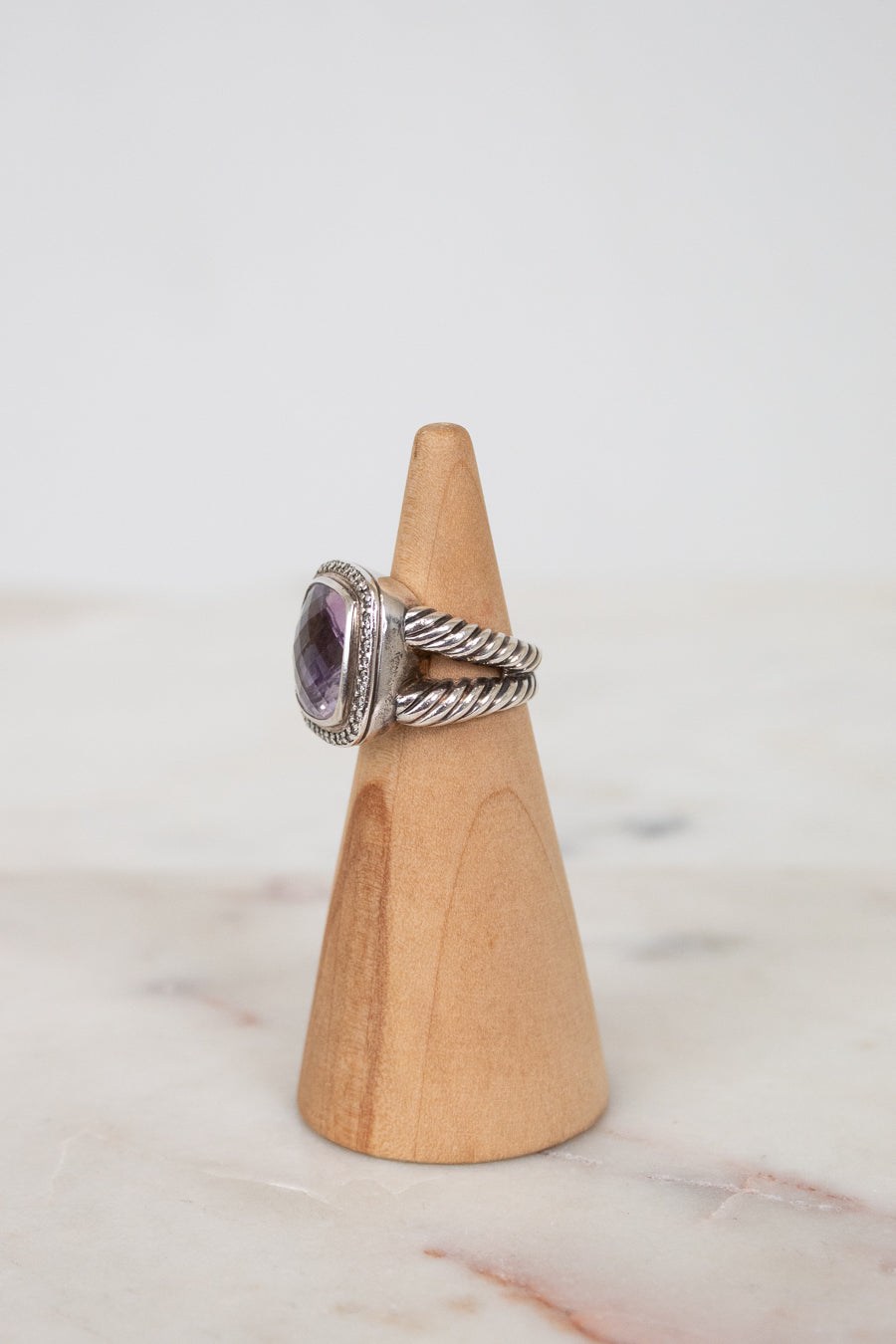 Silver ring with a purple gemstone on a wooden cone against a marble background