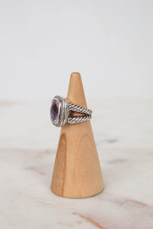 Silver ring with a purple gemstone on a wooden cone against a marble background