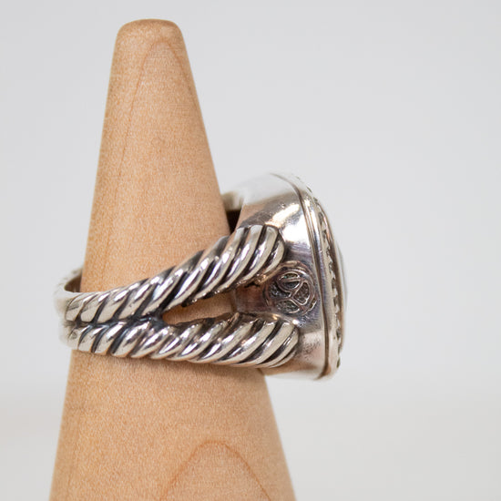Silver ring with twisted design on a wooden display block against a white background