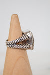Silver ring with twisted design on a wooden display block against a white background