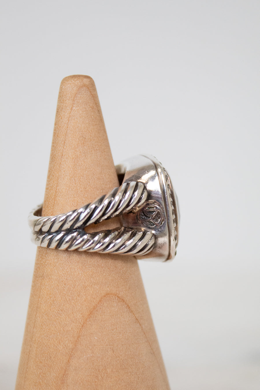 Silver ring with twisted design on a wooden display block against a white background
