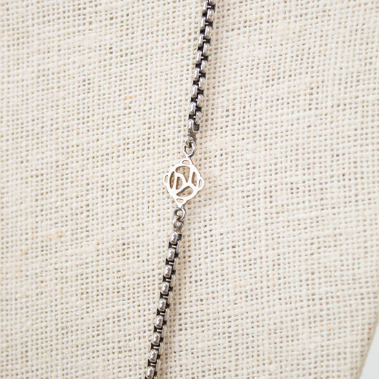 Silver necklace with a small logo on a beige fabric background