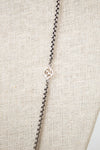 Silver necklace with a small logo on a beige fabric background