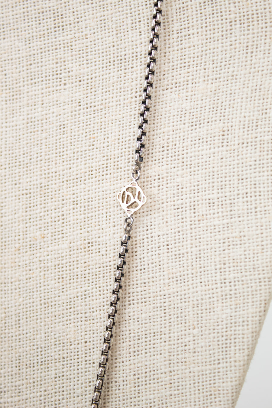 Silver necklace with a small logo on a beige fabric background