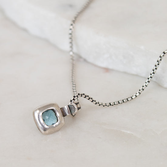Silver necklace with back of pendant on a light background