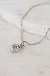 Silver necklace with back of pendant on a light background
