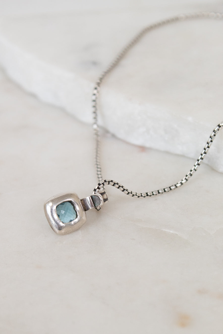 Silver necklace with back of pendant on a light background