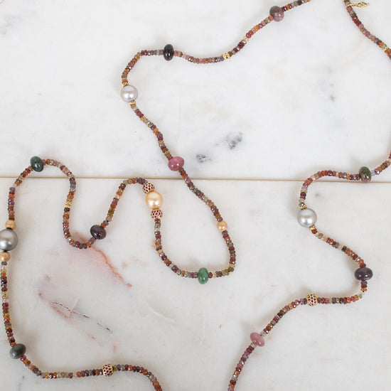 Necklace with autumnal colored, multi-sized beads laying along a marble background