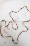 Necklace with autumnal colored, multi-sized beads laying along a marble background
