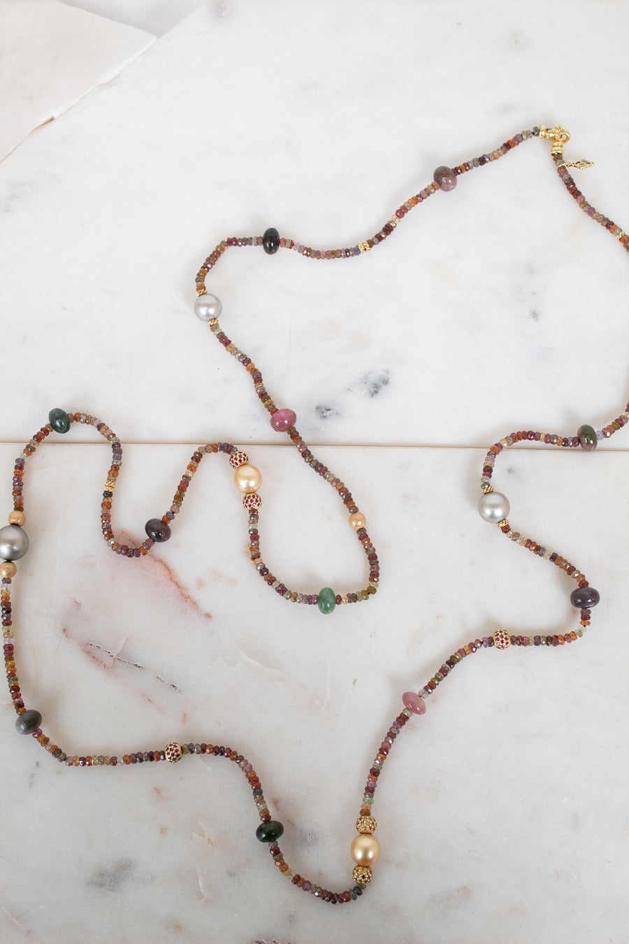 Necklace with autumnal colored, multi-sized beads laying along a marble background
