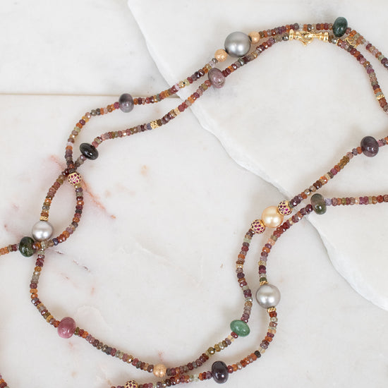 Close-up photo of layered necklace with different sized autumnal colored beads laying on a plain marble surface