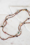 Close-up photo of layered necklace with different sized autumnal colored beads laying on a plain marble surface