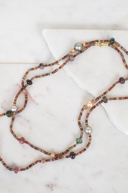 Close-up photo of layered necklace with different sized autumnal colored beads laying on a plain marble surface