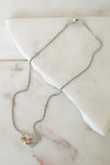 A delicate silver box chain necklace with a two-tone pendant featuring a gold and silver interlocked ring design, displayed on a white marble slab.