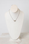 A silver chain necklace with a small interlocked rings pendant displayed on a cream-colored fabric jewelry bust against a light gray background.