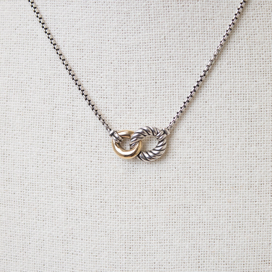 Interlocking gold and ribbed silver rings attached to dainty box chain necklace displayed against a plain textured background