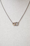 Interlocking gold and ribbed silver rings attached to dainty box chain necklace displayed against a plain textured background