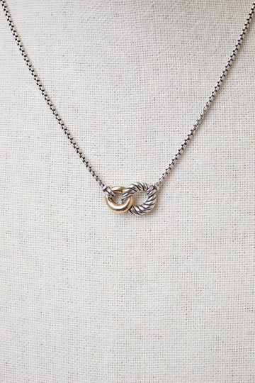 Interlocking gold and ribbed silver rings attached to dainty box chain necklace displayed against a plain textured background