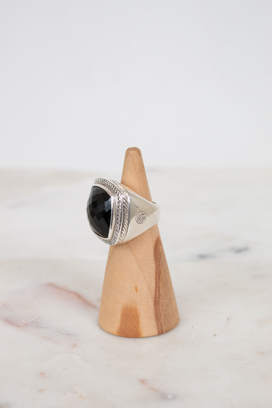 A silver ring with a large black stone, displayed on a small wooden cone stand against a light gray background.