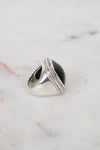 A silver signet-style ring with a large oval black stone, photographed on a light marble surface.