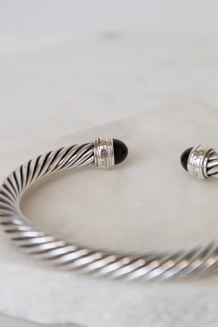 A silver cable-wrapped cuff bracelet with black onyx stone end caps, resting on a light marble surface.