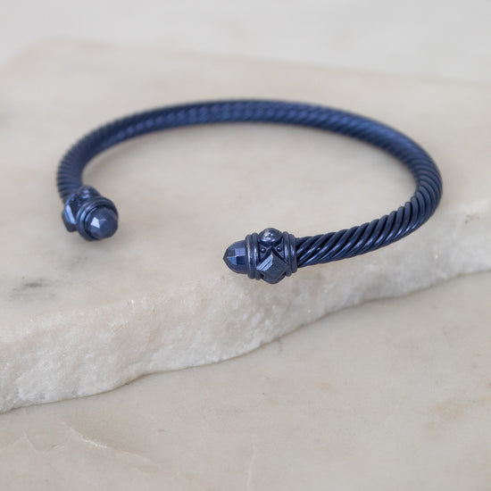 Navy blue bracelet with decorative ends on a light stone surface