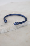 Navy blue bracelet with decorative ends on a light stone surface