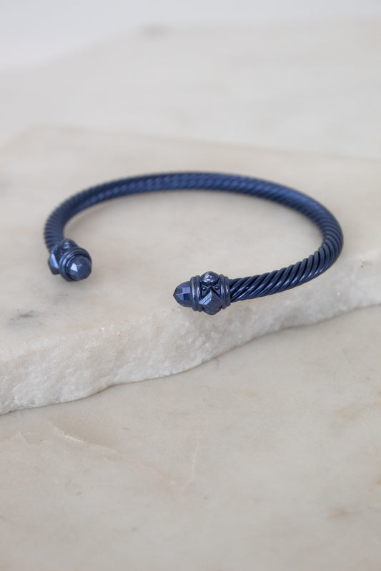 Navy blue bracelet with decorative ends on a light stone surface