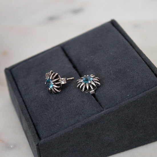 Pair of silver starburst shaped earrings with blue stones on a gray jewelry box.