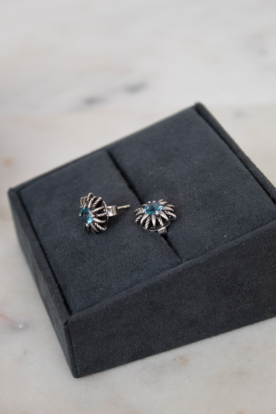 Pair of silver starburst shaped earrings with blue stones on a gray jewelry box.