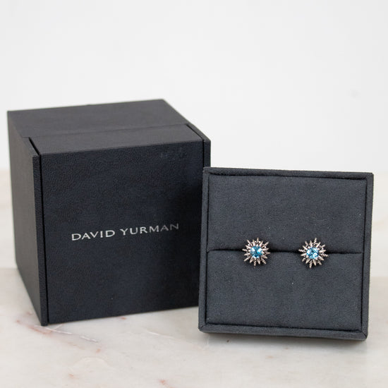 Silver starburst shaped earrings with blue stone in center. 