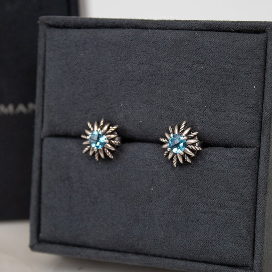 Pair of starburst-shaped earrings with blue gemstones in center sitting on a black jewelry box.