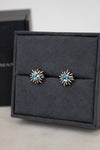 Pair of starburst-shaped earrings with blue gemstones in center sitting on a black jewelry box.