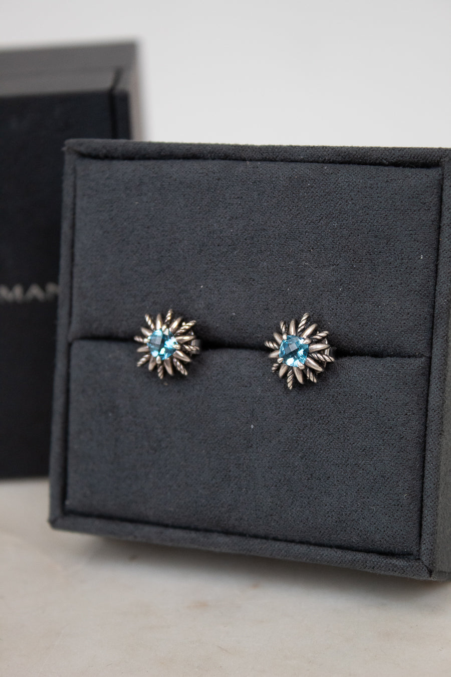 Pair of starburst-shaped earrings with blue gemstones in center sitting on a black jewelry box.