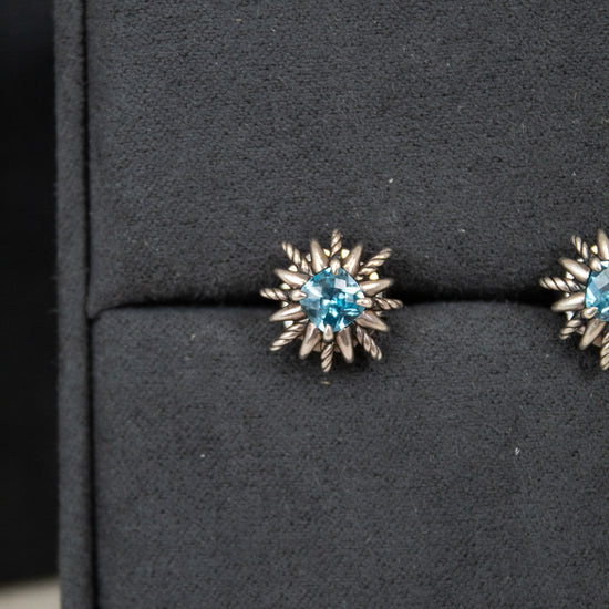 Pair of starburst-shaped earrings with blue gemstones on a black display box.