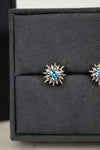 Pair of starburst-shaped earrings with blue gemstones on a black display box.