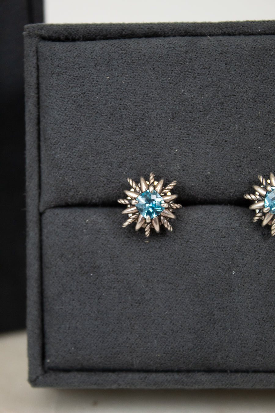 Pair of starburst-shaped earrings with blue gemstones on a black display box.